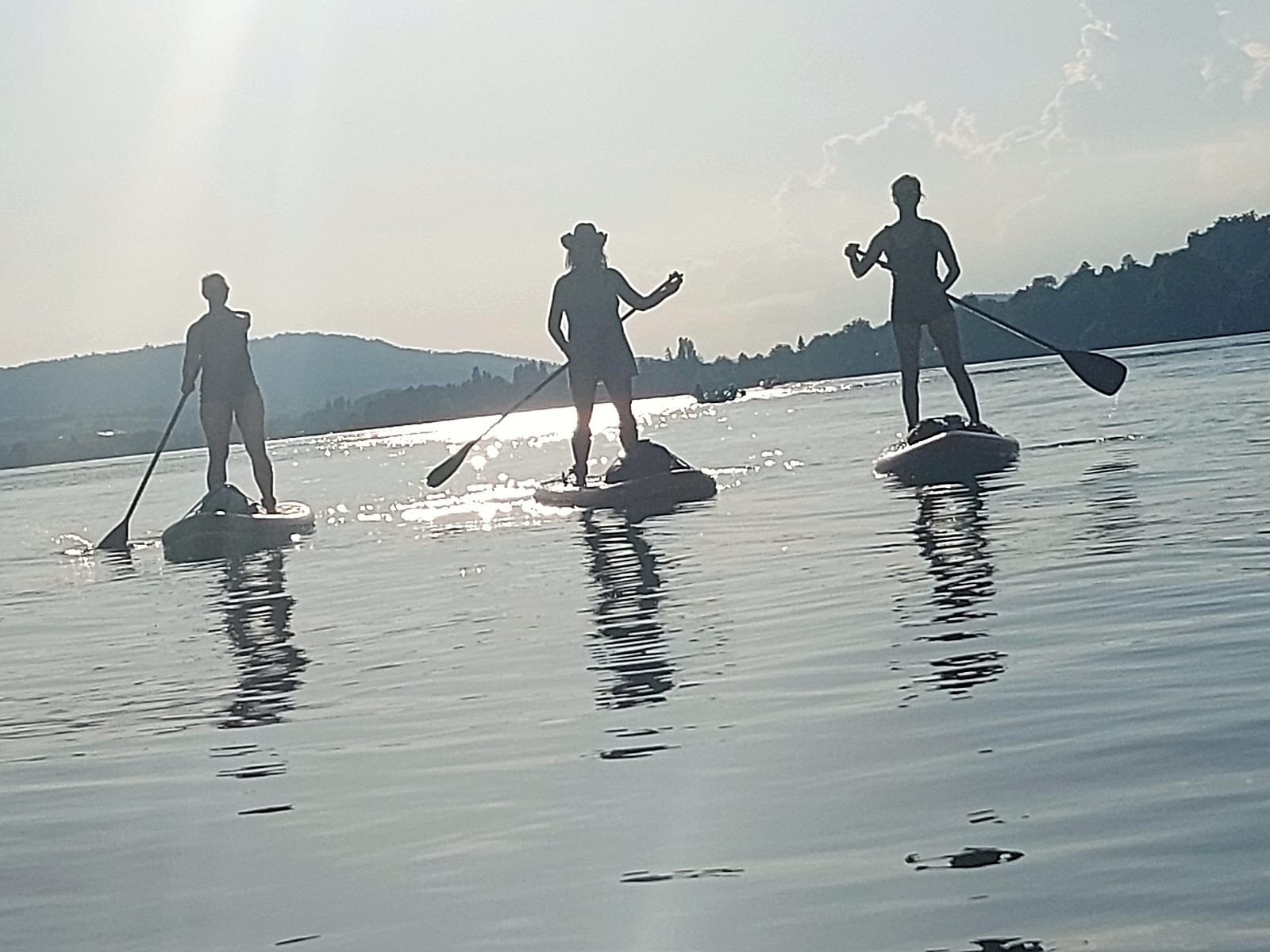 Drei Paddler als Silhouetten auf spiegelglattem Wasser vor den Bergen