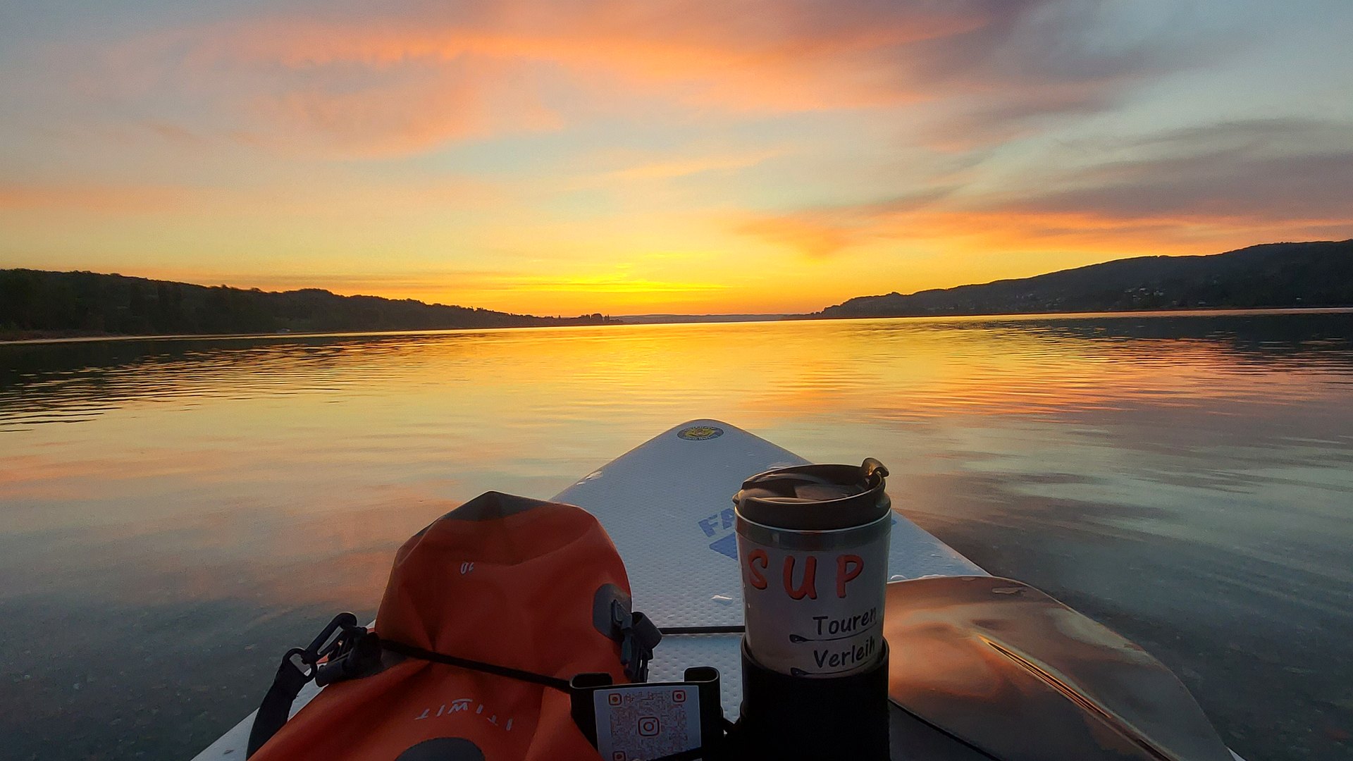Sonnenuntergang über dem Untersee, vom Board aus gesehen: Bugspitze des SUP, Drybag und Thermobecher im Vordergrund