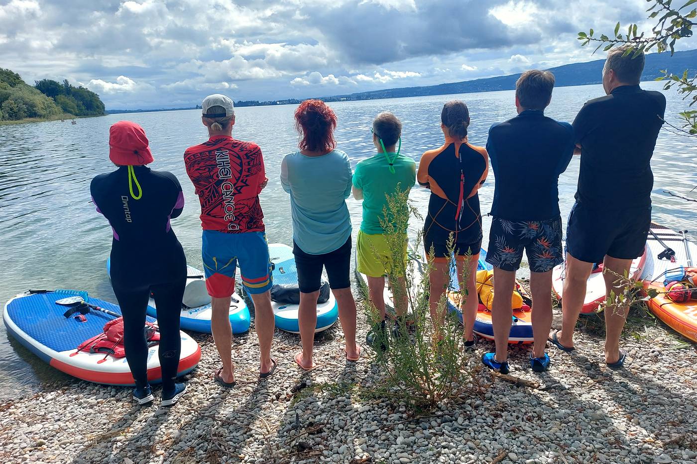 Gruppe steht am Ufer vor einer Reihe aufgereihter SUP-Boards