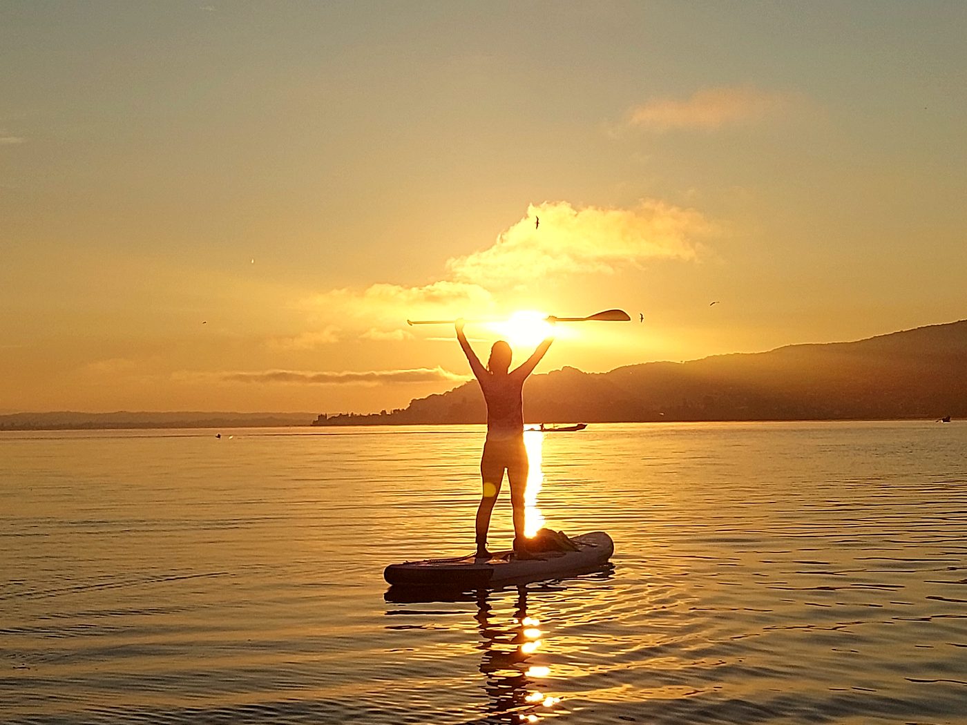 Paddler mit erhobenen Armen vor der untergehenden Sonne auf dem Untersee