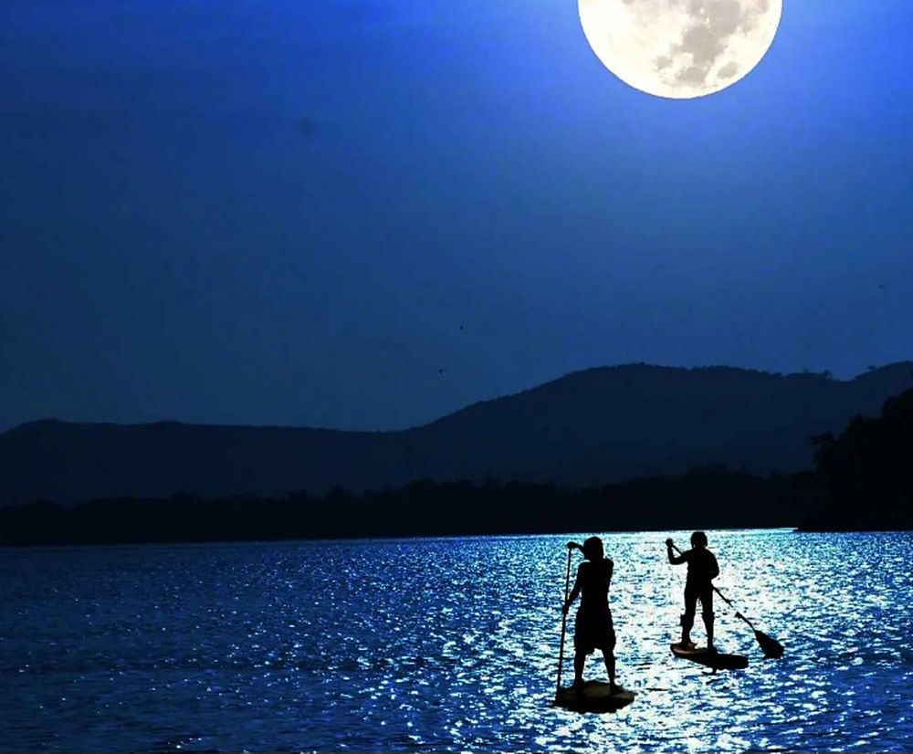 Zwei Paddler als Silhouetten auf dem mondbeschienenen See, darüber der Vollmond